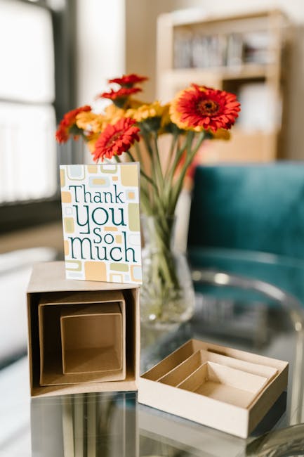 A 'Thank You So Much' card with red and yellow flowers and open packaging on a glass table.