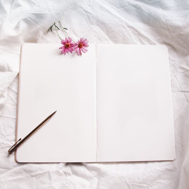 Open notebook with pen and pink flowers on white cloth, perfect for ideas or journaling.